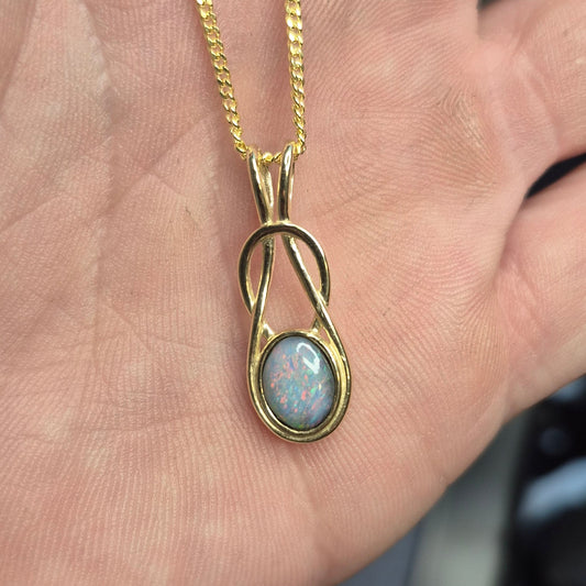 Gold necklace with a pendant featuring an opal stone held in a hand.